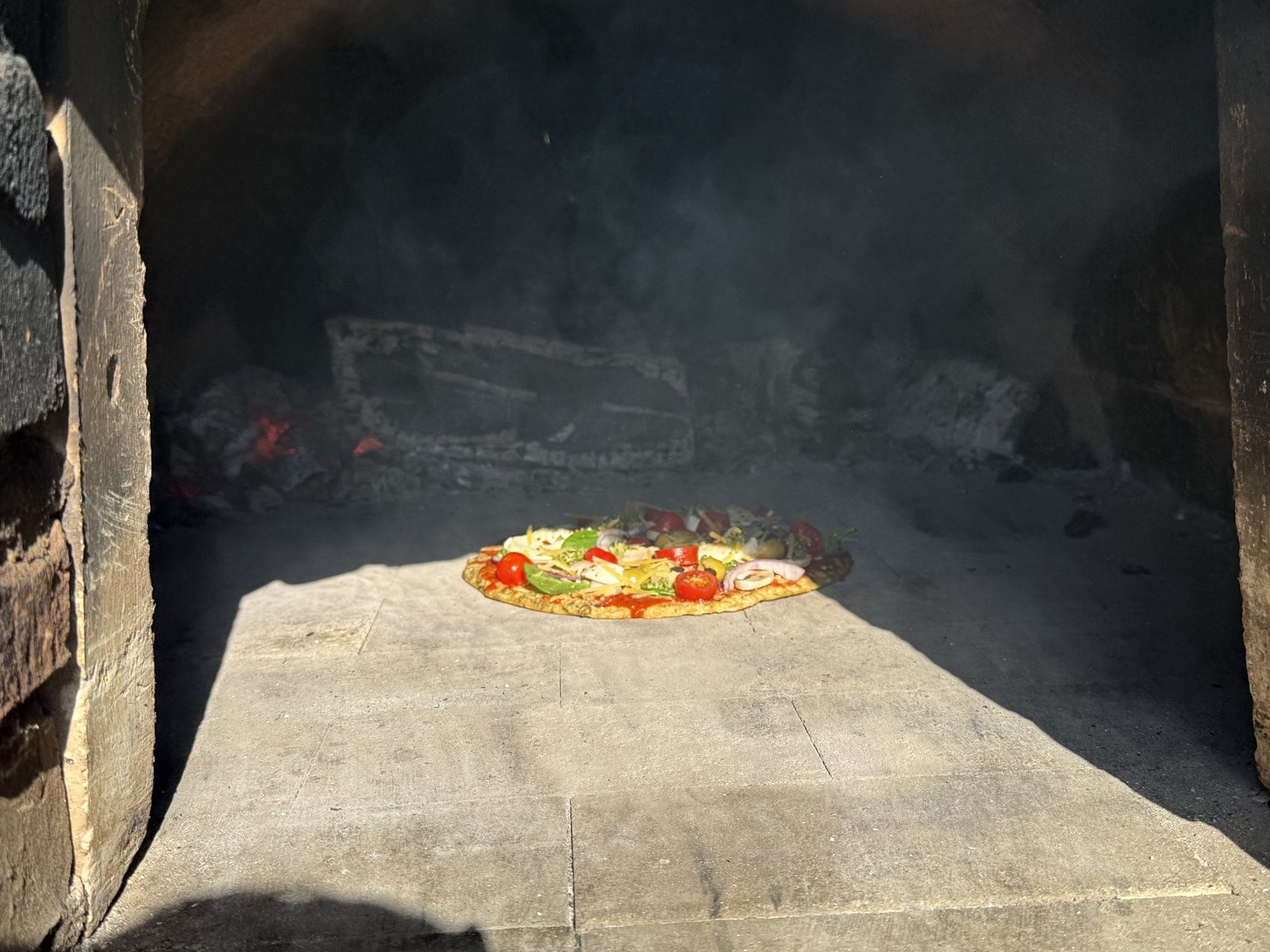 Een pizza met groenten op de stenen vloer van een houtgestookte steenoven.